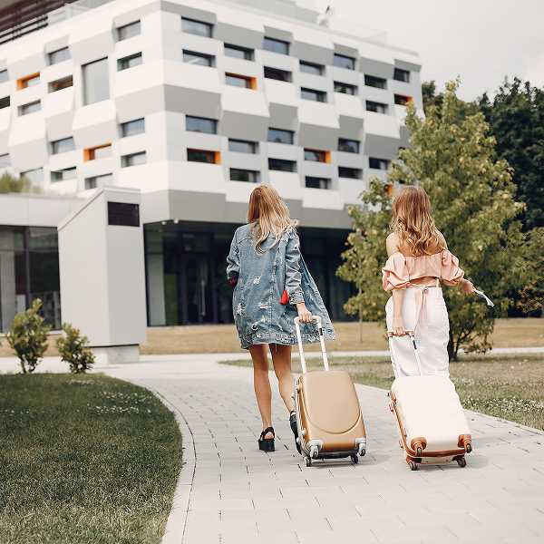 Two women with luggage walking down a path near condos available for rent.