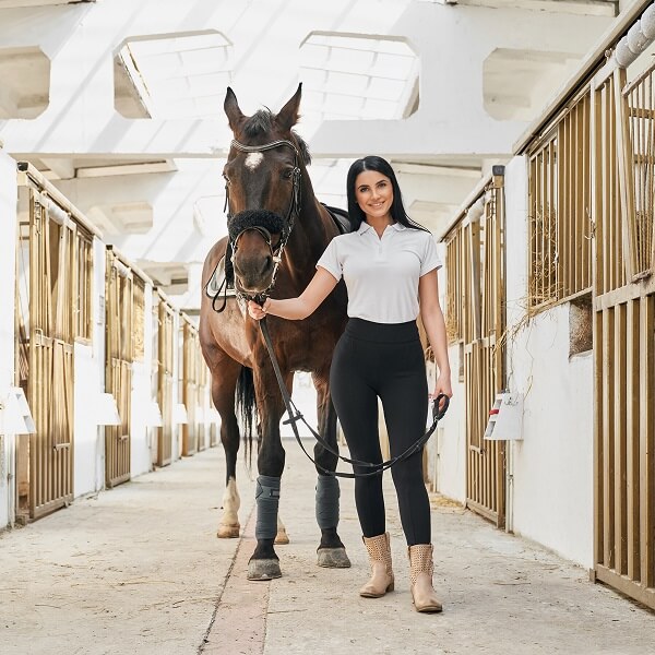 Une femme en chemise blanche et pantalon noir se tient à côté d'un cheval