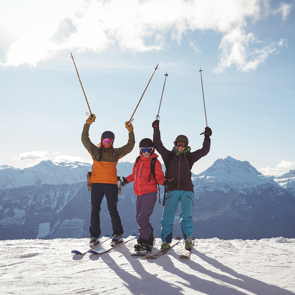Trois skieurs se tiennent au sommet d'une montagne à Ski à Orford, admirant le paysage enneigé.