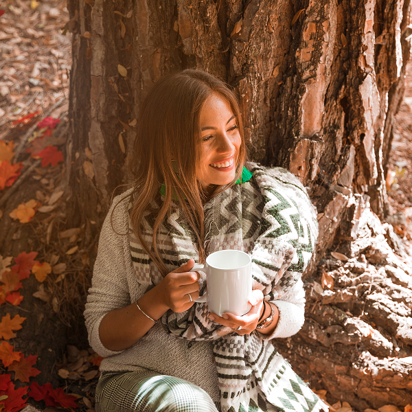 Une femme assise dans les feuilles, tenant une tasse, évoquant un moment de détente en pleine nature.
