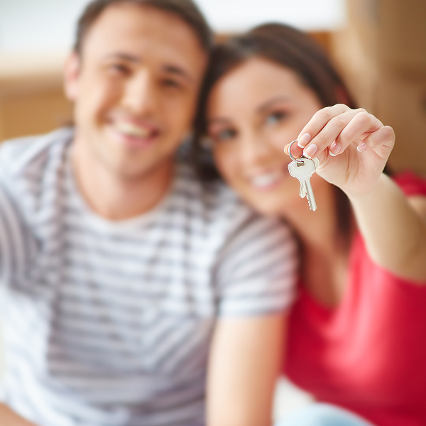 A man and woman sit on the floor, holding a key, discussing a condo for rent.