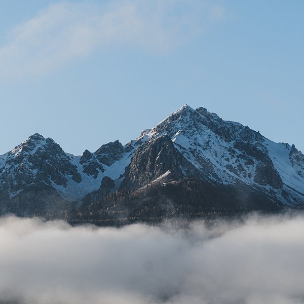 A plane flying over Mont-Orford mountain range, surrounded by fluffy clouds in a clear blue sky.
